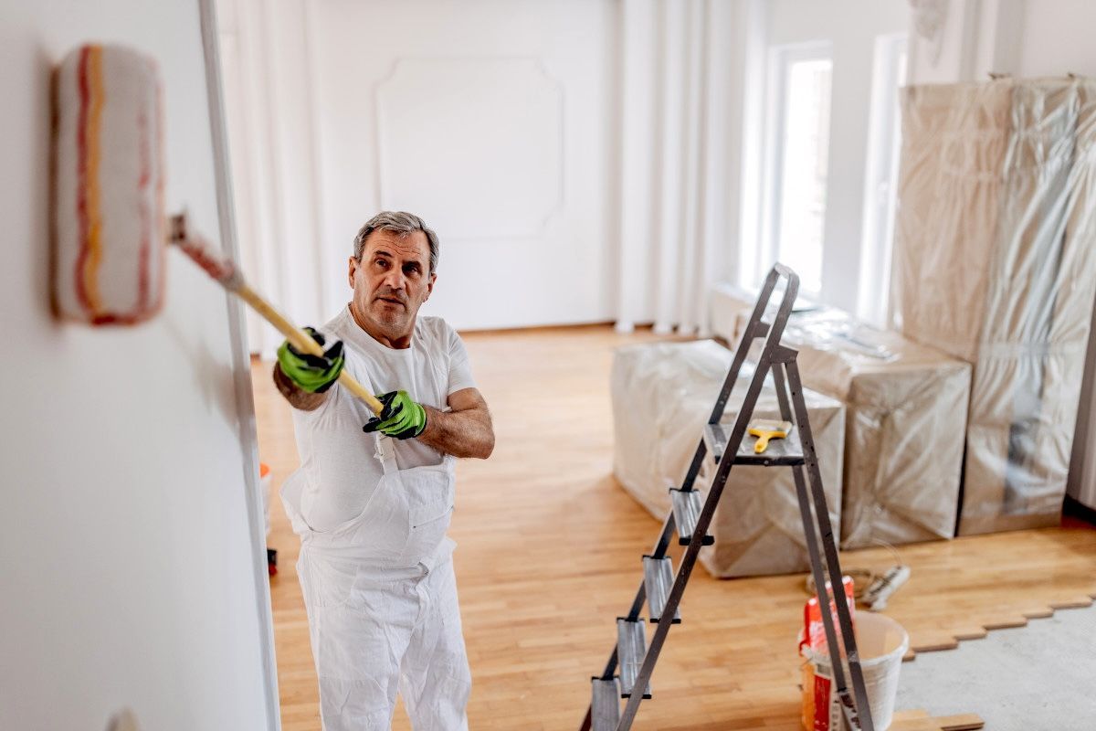 Foxglove Decor interior painter in white overalls painting a Sunderland wall with a roller, ladder nearby.