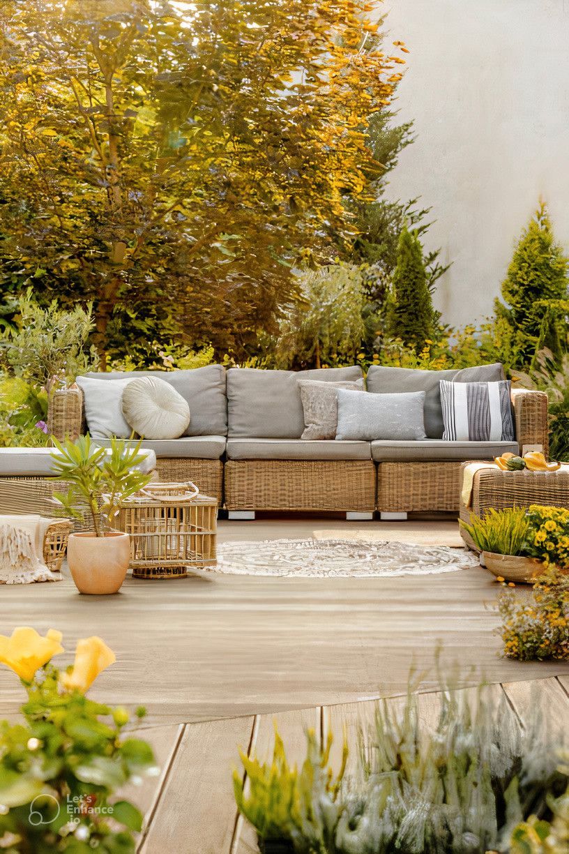 A wicker couch is sitting on a wooden deck in a garden.