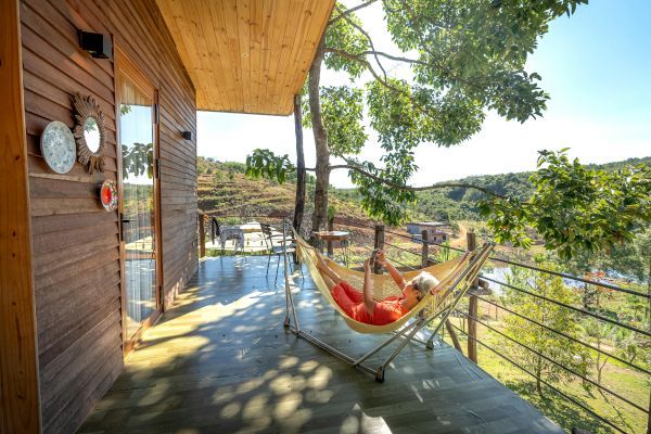 A person is laying in a hammock on the porch of a house.