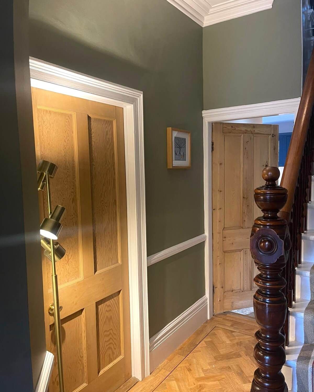 Hallway with olive green walls, light wood doors, and a dark wooden staircase.