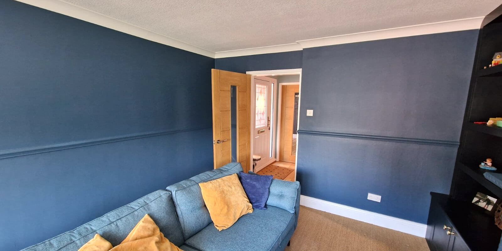 A living room with blue walls, a blue sofa with yellow pillows, and a doorway.