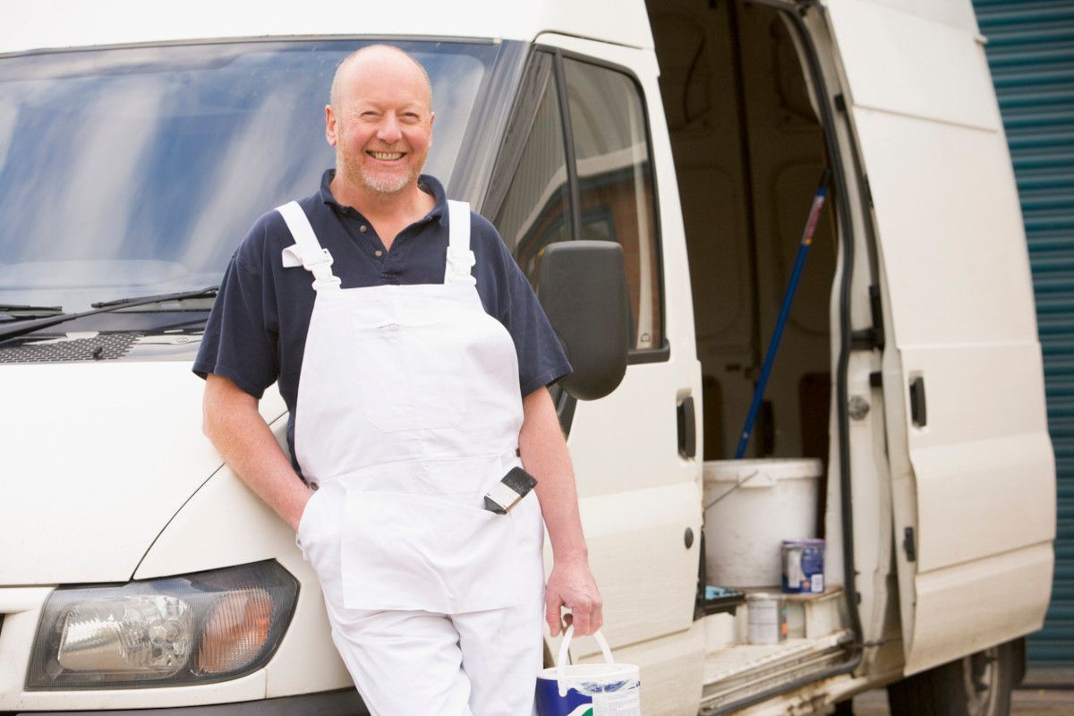 Sunderland painter smiles, holding brush and paint bucket, wearing overalls, next to Foxglove Decor van.