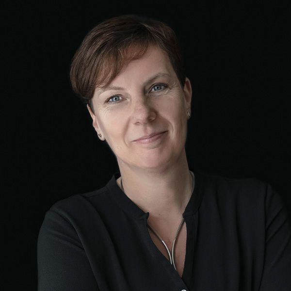 Natalie draagt een zwart shirt en een ketting en lacht naar de camera.