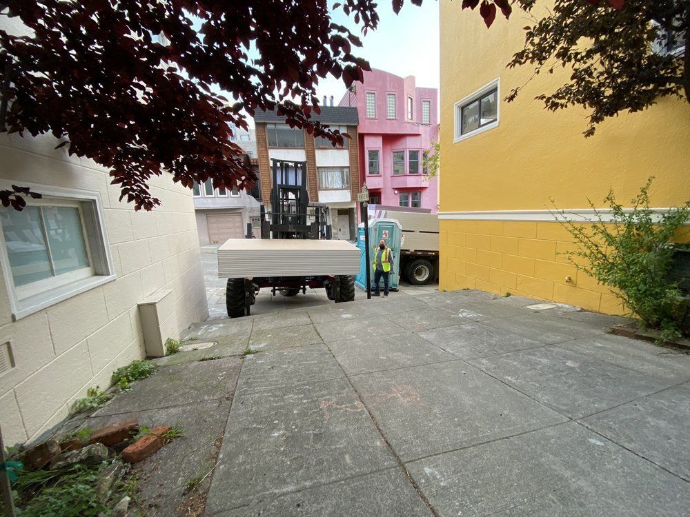 Two construction workers are carrying a large piece of drywall in a room.