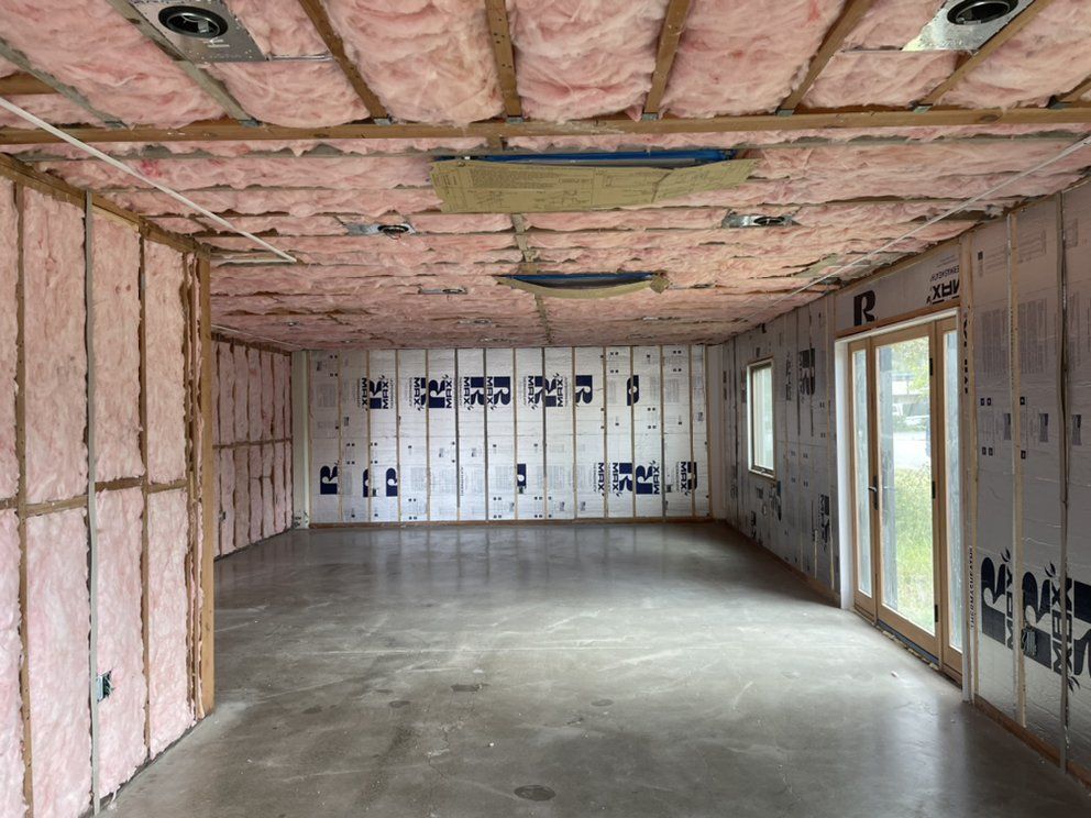 A man is standing on a ladder insulating a wall.