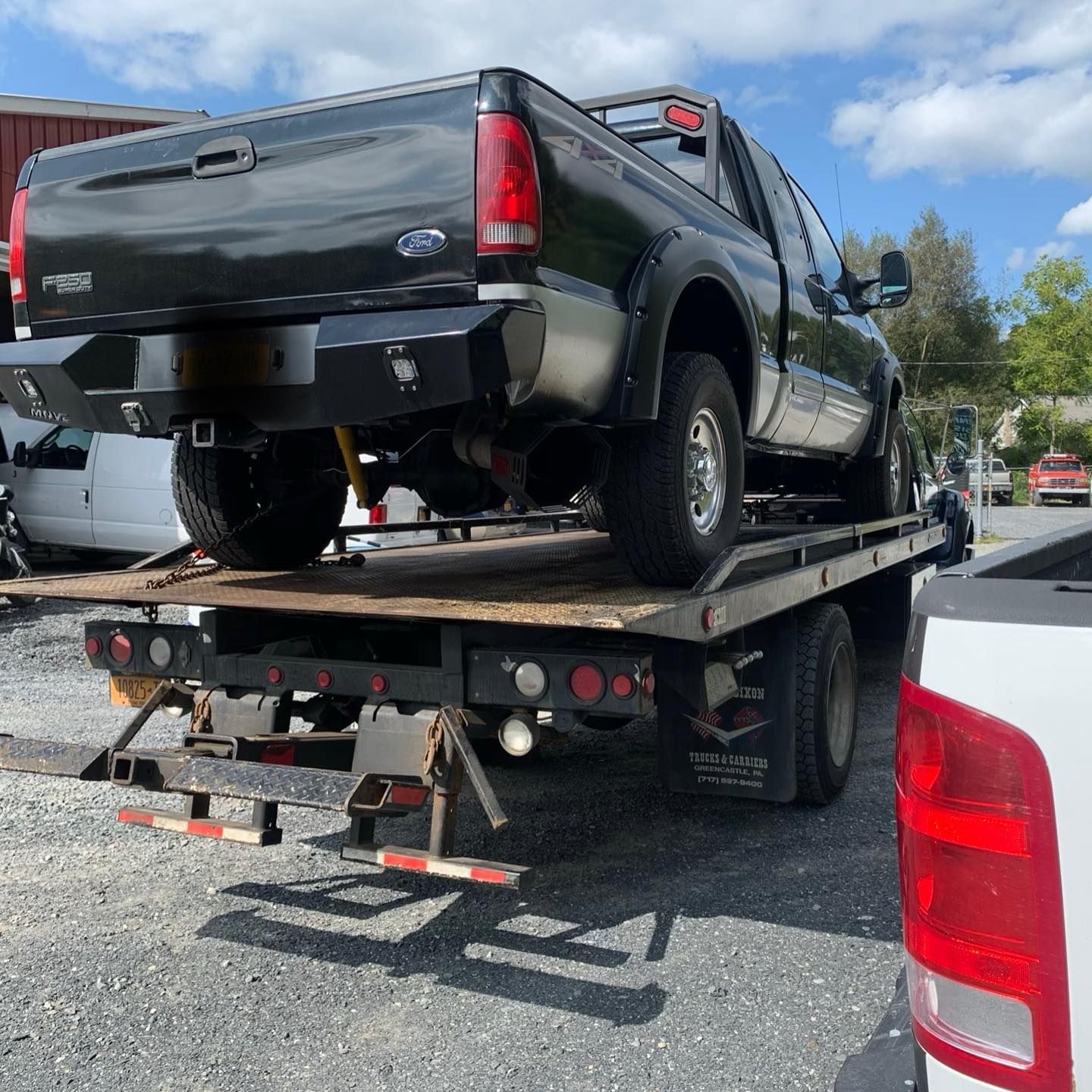Black Ford truck on a flatbed tow truck outdoors on a sunny day.
