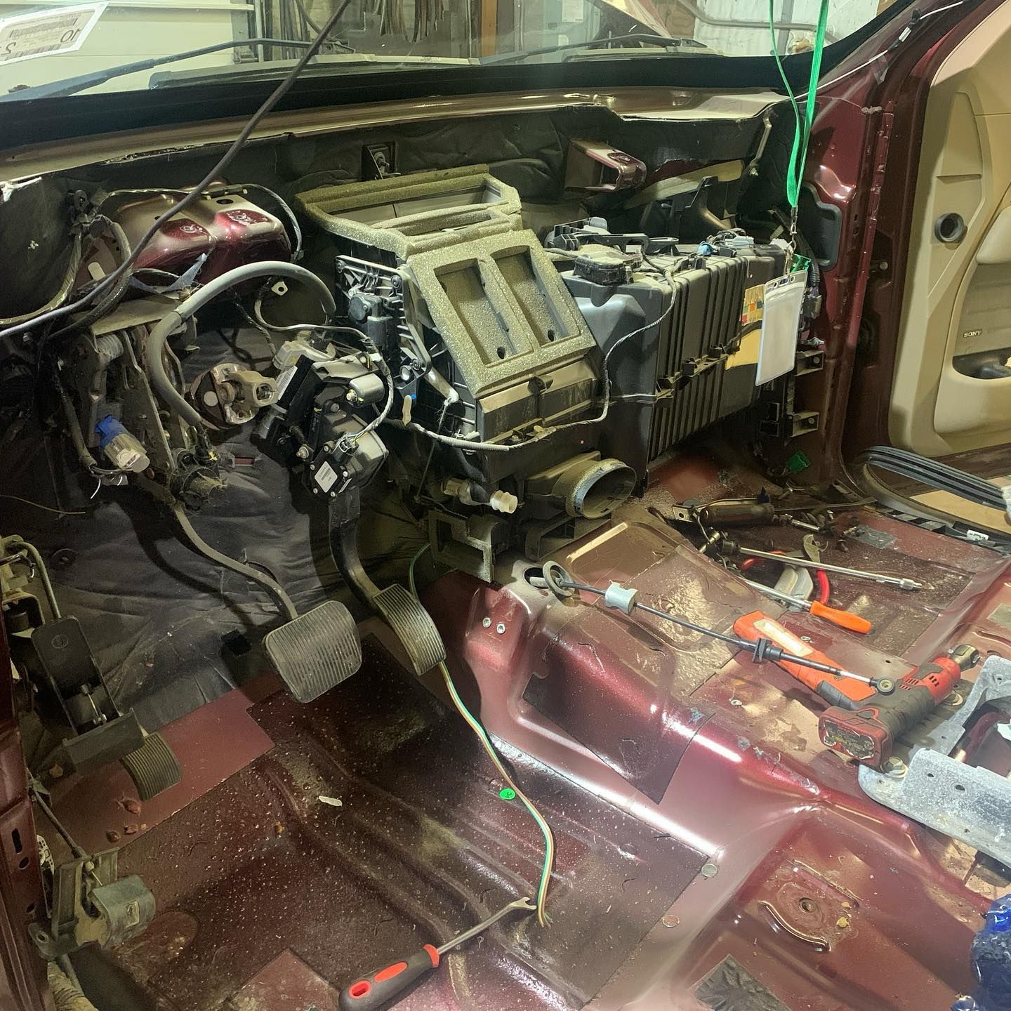 Interior of a car with dashboard components removed, revealing air conditioning system, wires, and tools on a maroon floor.