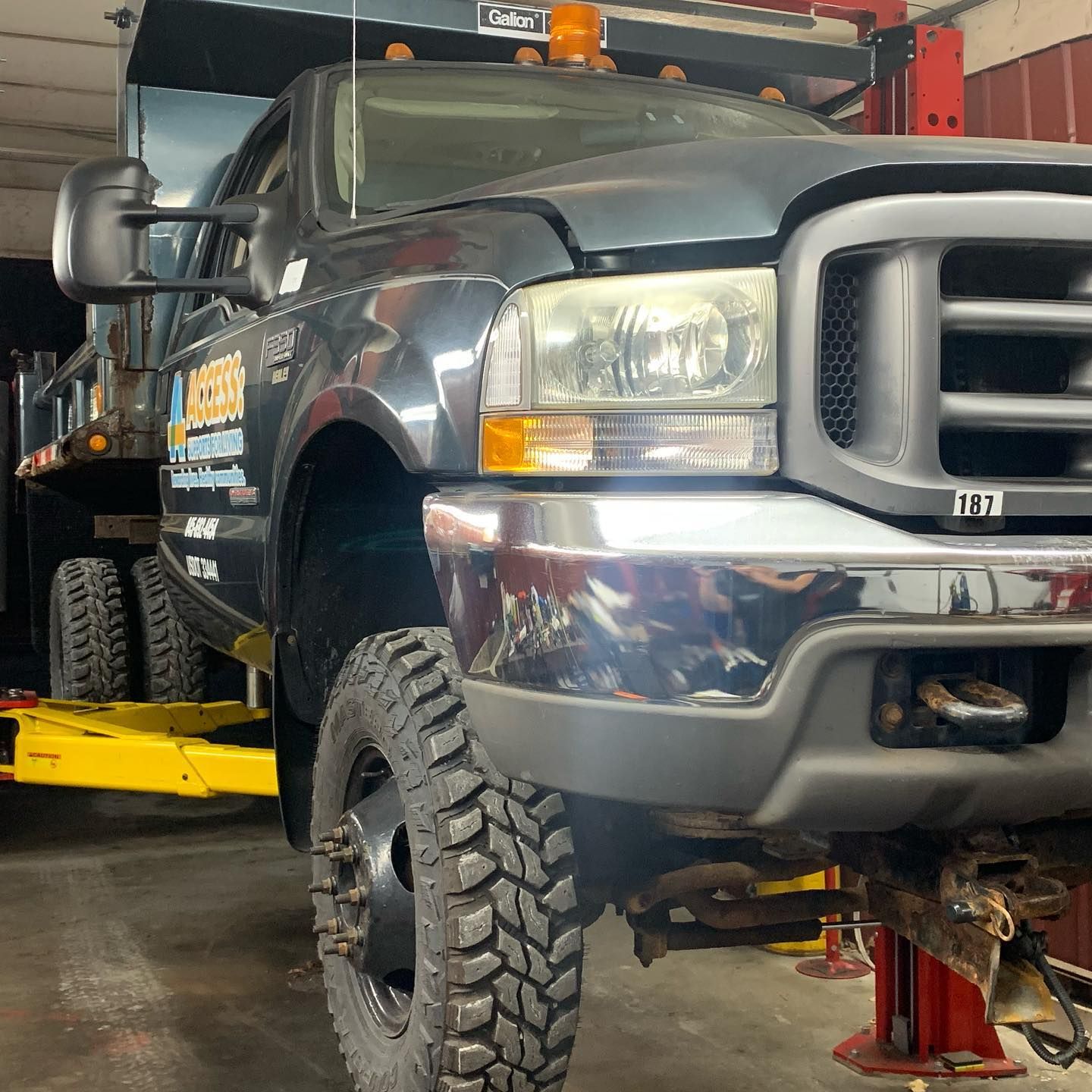 Dark gray dump truck on a lift inside a repair shop, the front tire is in focus.