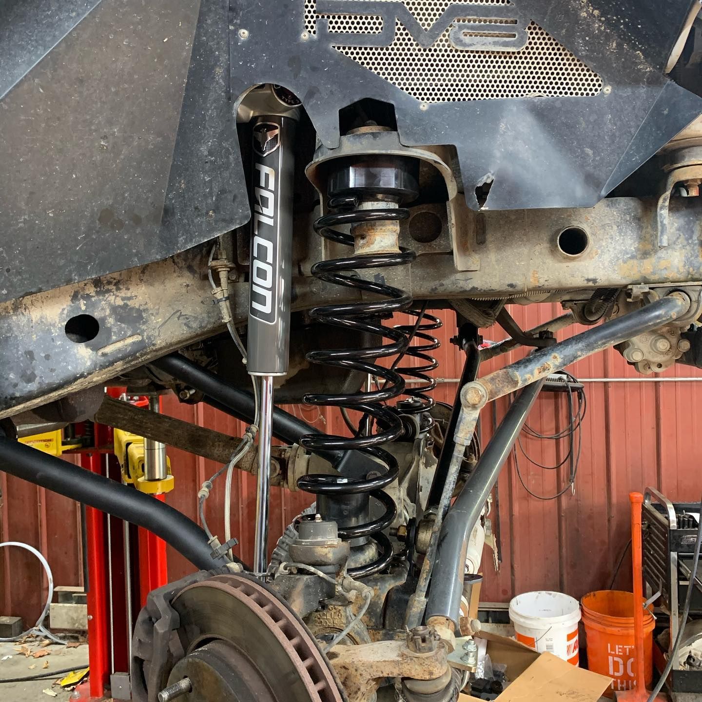 Jeep suspension components: shock absorber, coil spring, control arm, brake rotor, and a metal shield in a garage setting.