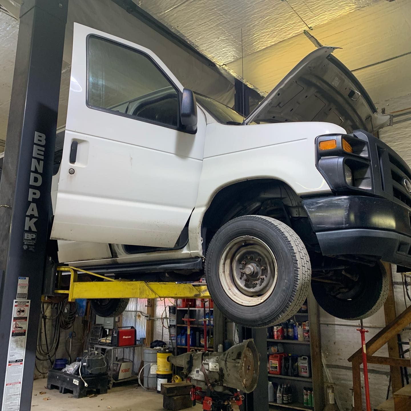 White van on a lift in a garage with the hood open and door ajar.