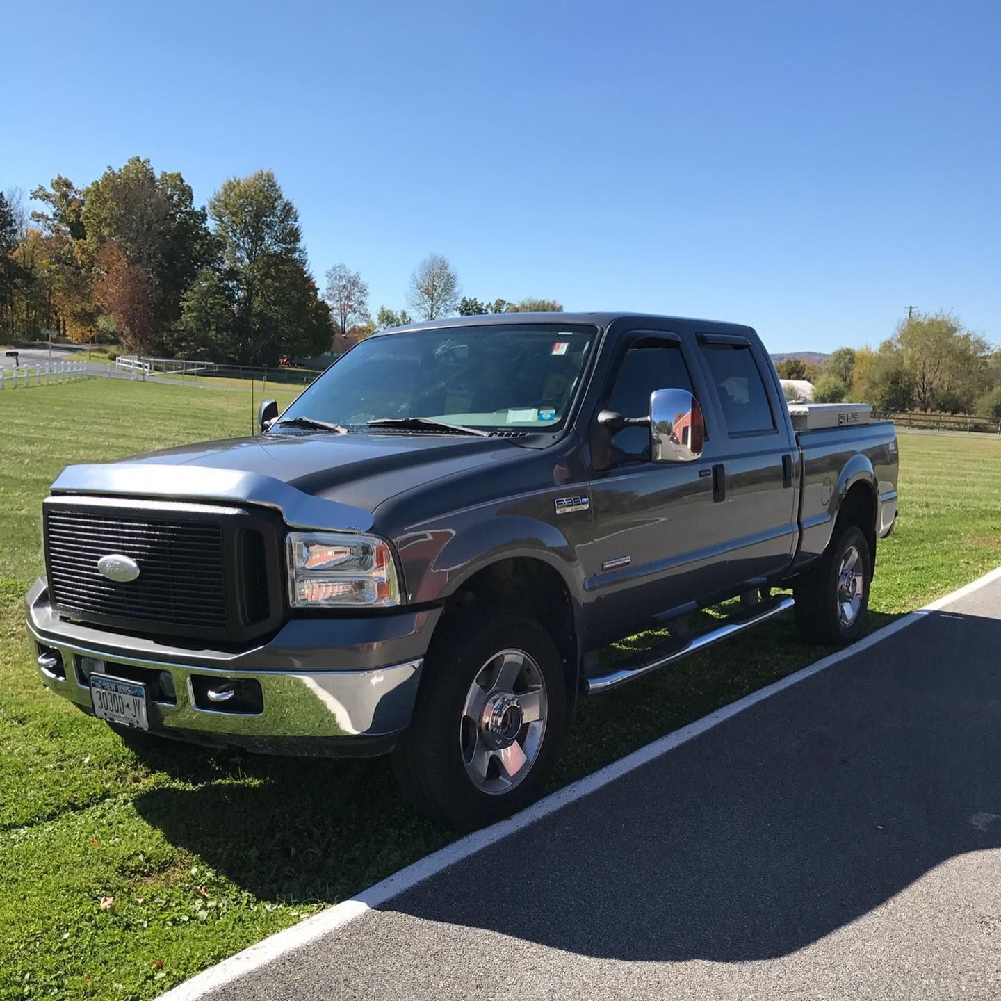 Dark gray Ford F-250 pickup truck parked on grass near a sidewalk under a blue sky.