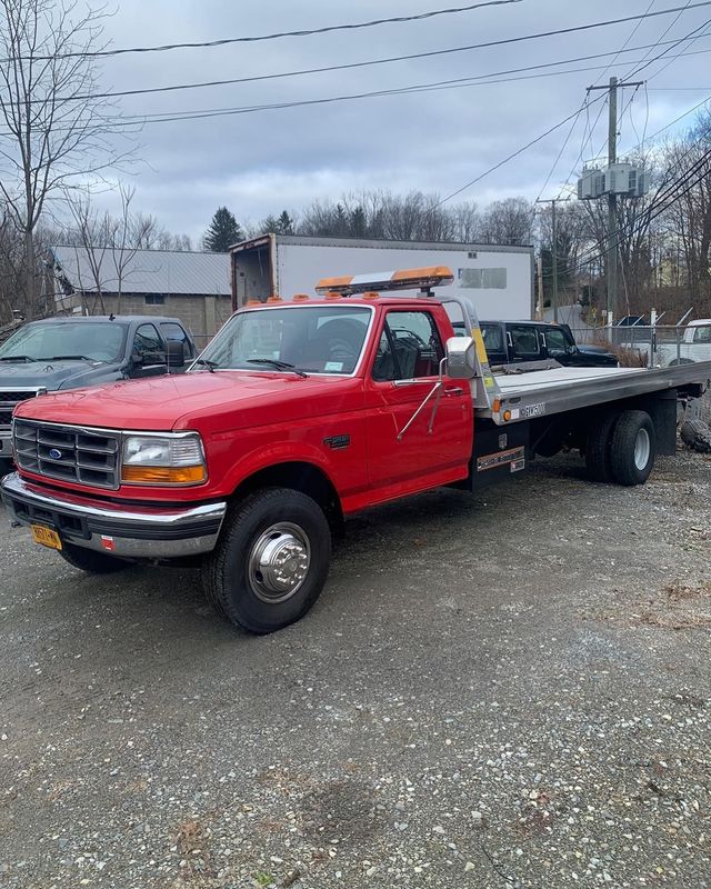 Red tow truck parked on gravel, with a flatbed and an orange light bar. Red tow truck parked on gravel, with a flatbed and an orange light bar.