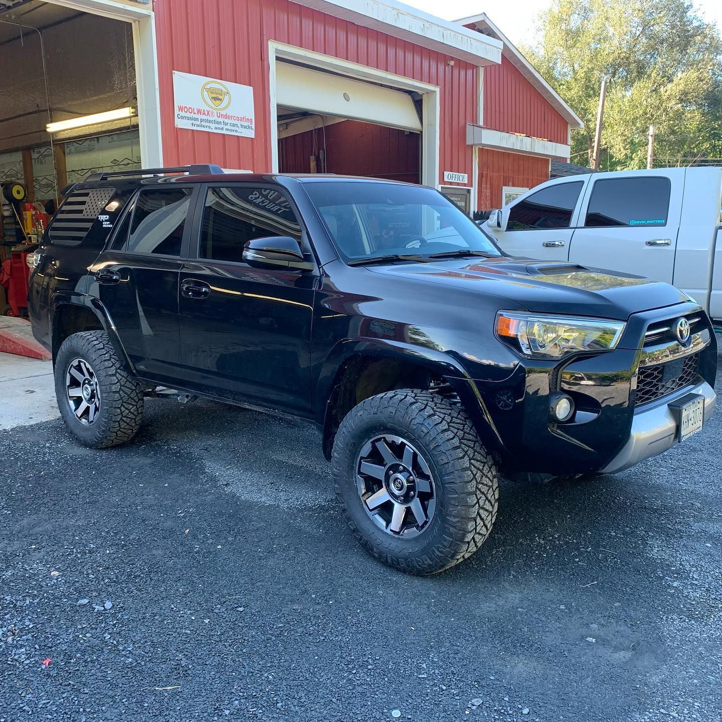 Black Toyota 4Runner SUV parked on gravel in front of a red building with a garage door.