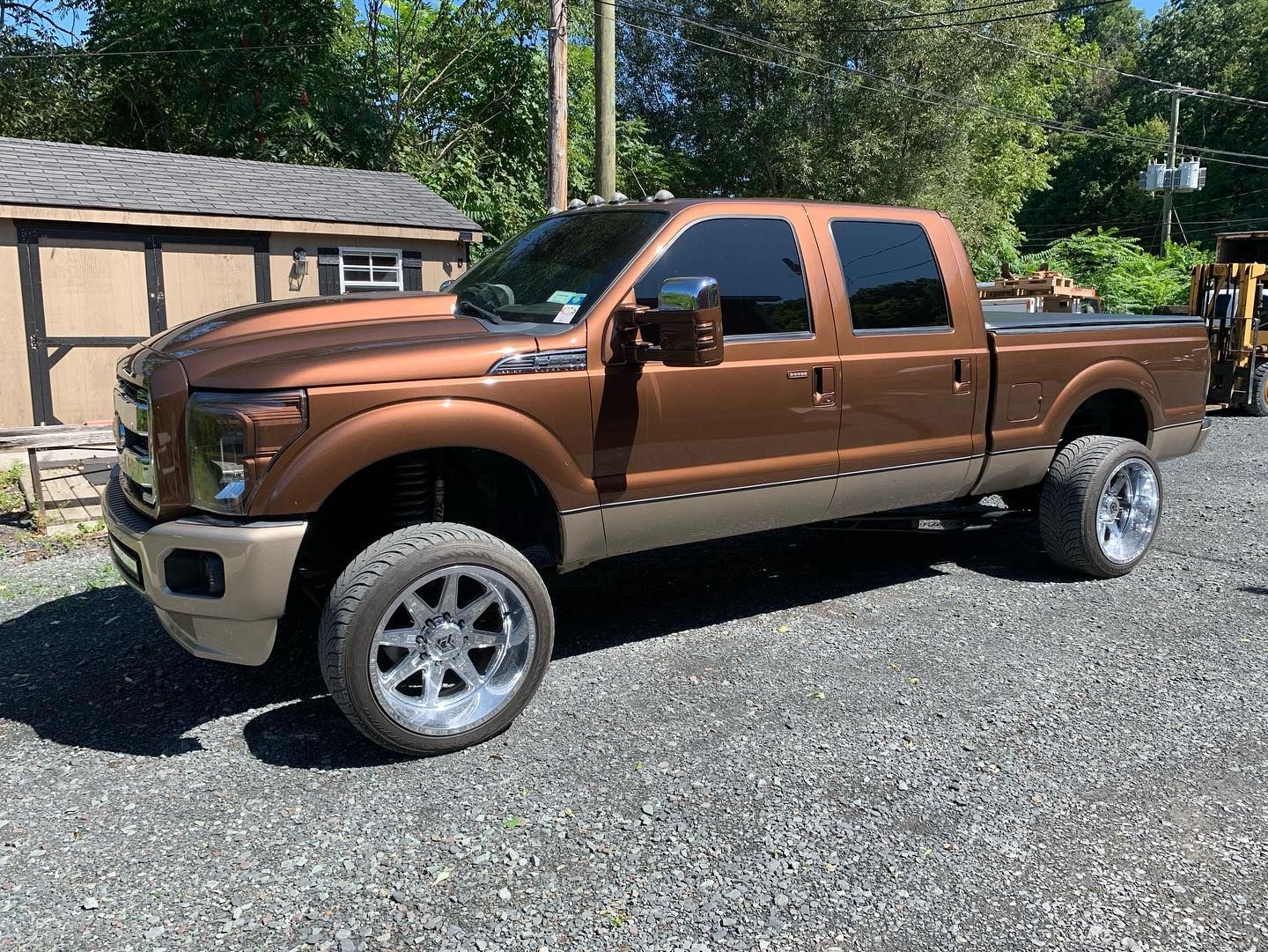 Brown and tan Ford truck with chrome wheels parked on gravel.