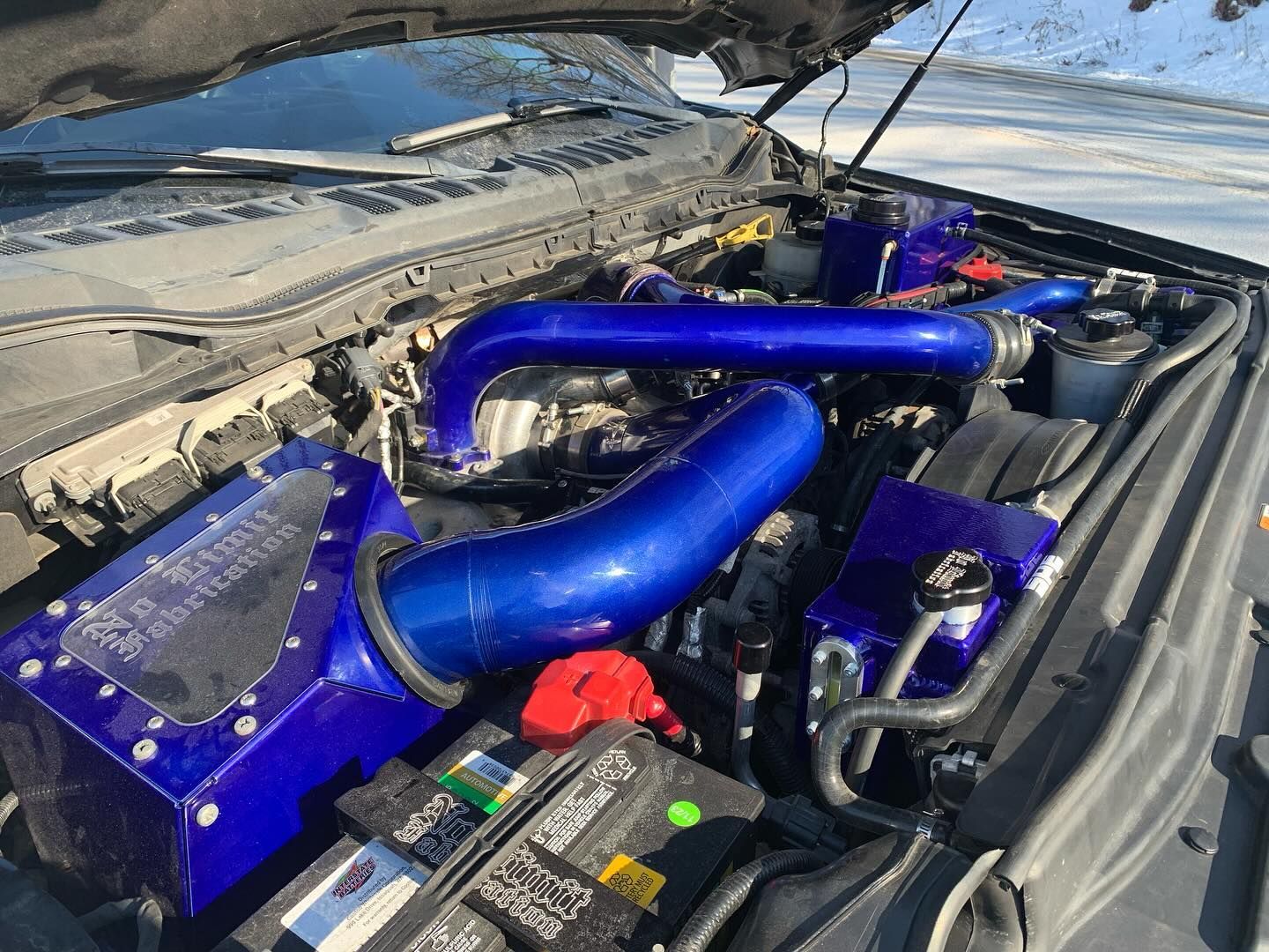 Blue-modified truck engine bay with custom air intake and piping, open hood, outdoors.