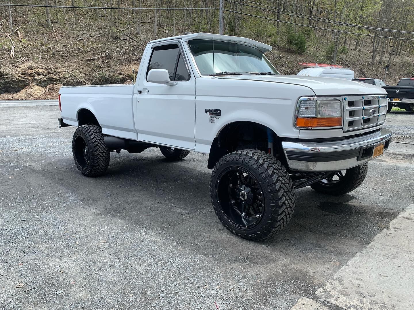 White Ford pickup truck with large black wheels parked on gravel. White Ford pickup truck with large black wheels parked on gravel.