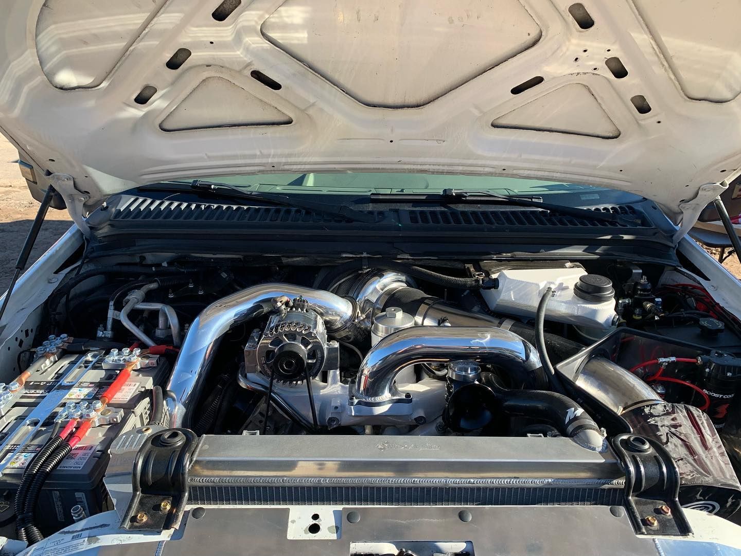 Open hood of a white truck, revealing a customized engine with chrome components.