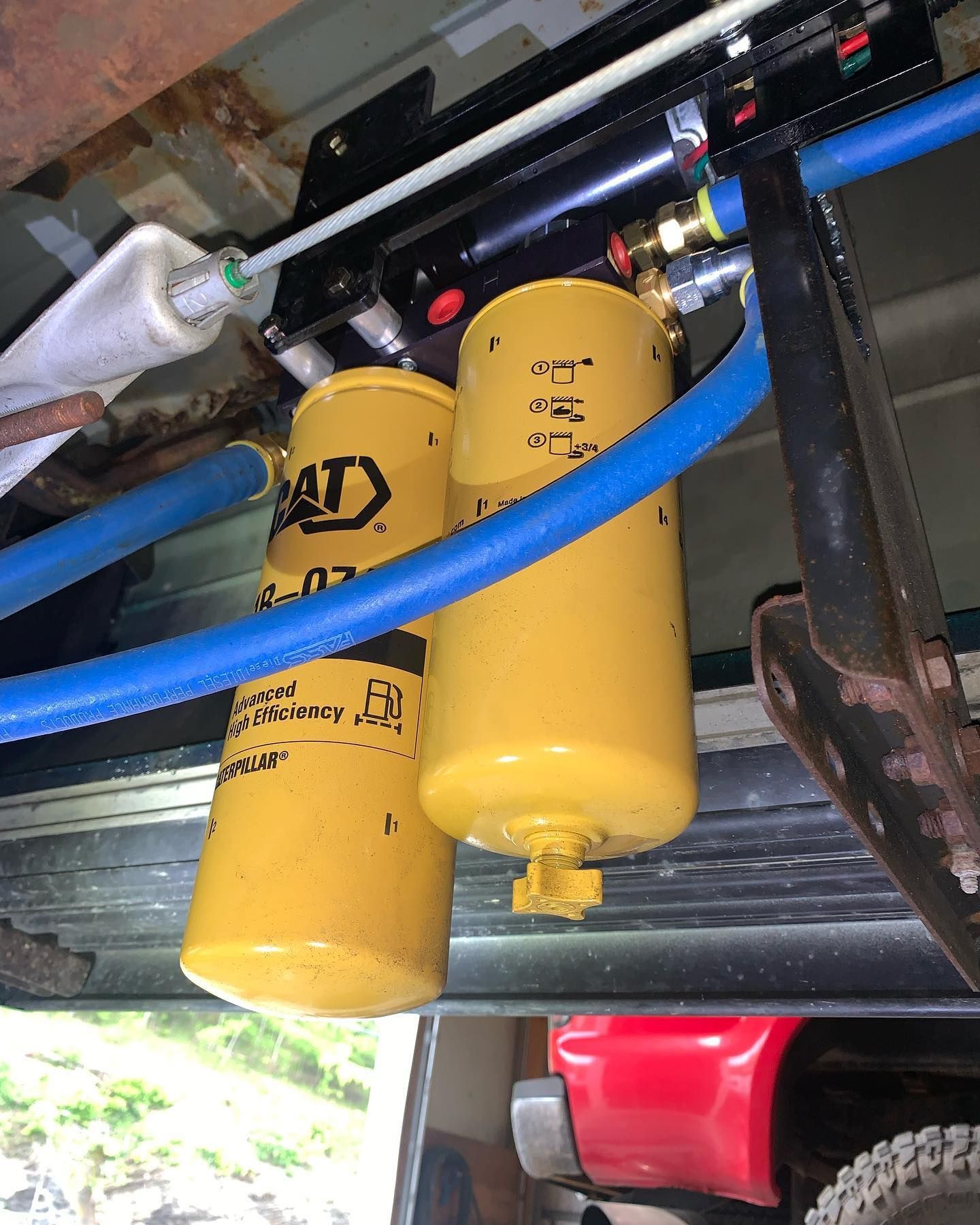 Two yellow CAT fuel filters mounted beneath a vehicle, connected with blue tubing and black hardware.