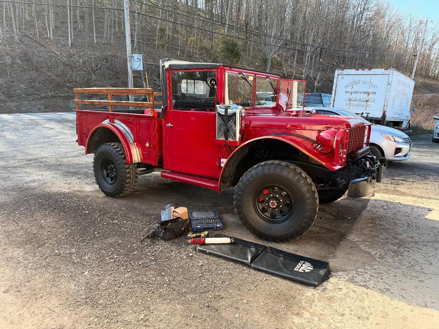 Red vintage pickup truck with black wheels, parked outdoors on gravel.