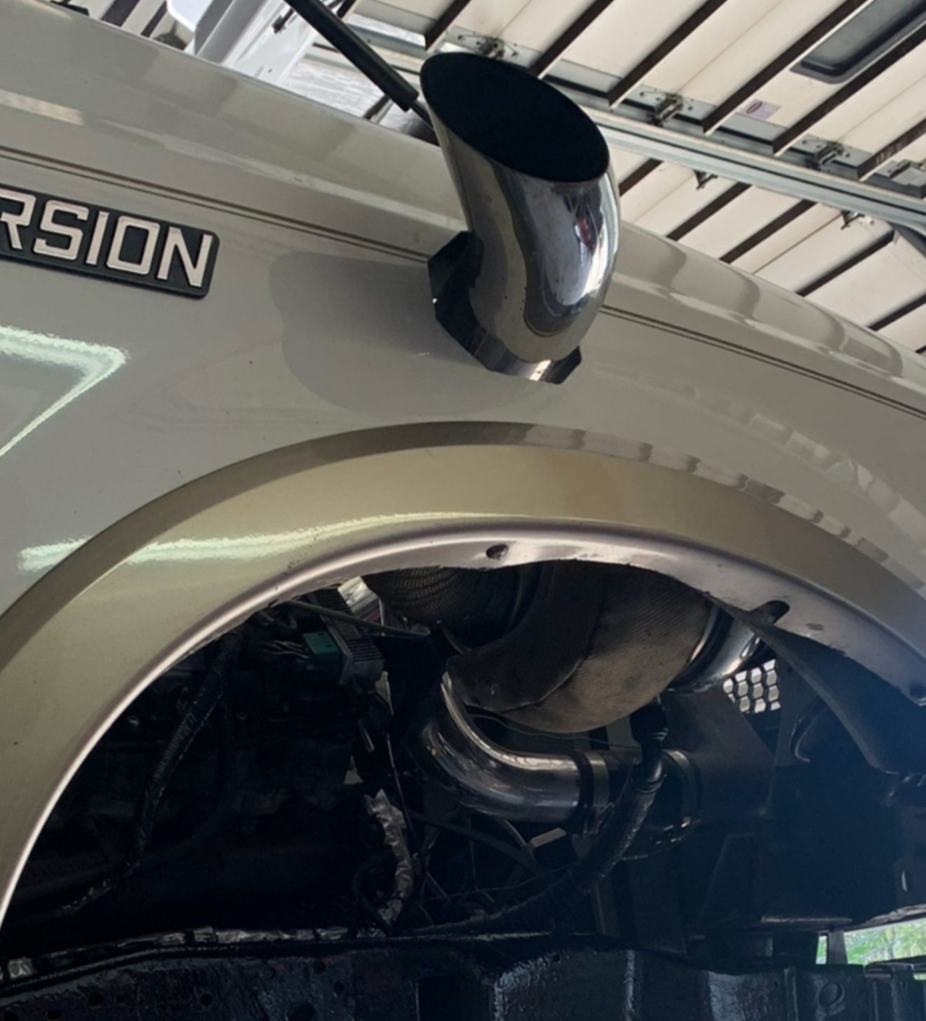 Close-up of a blue car's exhaust pipes. Two circular chrome pipes emerge from the car's underside.