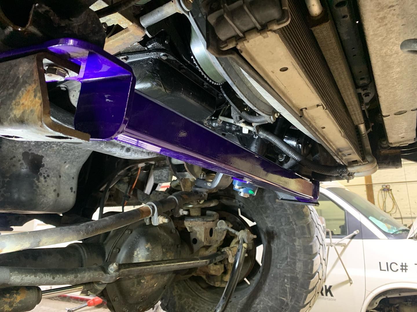 Underside of a vehicle, showing a purple-painted metal part, suspension components, tire, and radiator. Underside of a vehicle, showing a purple-painted metal part, suspension components, tire, and radiator.