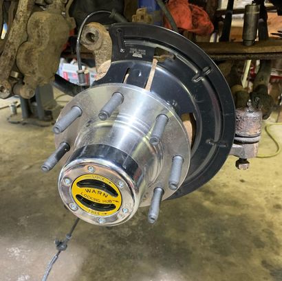 A shiny metal wheel hub with a yellow WARN emblem attached to a vehicle's front suspension. A shiny metal wheel hub with a yellow WARN emblem attached to a vehicle's front suspension.