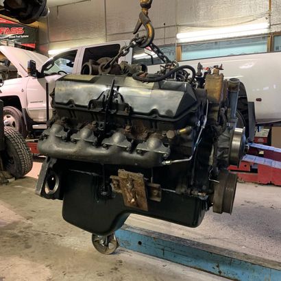 Engine suspended from a hoist in a garage, near a white truck. Engine suspended from a hoist in a garage, near a white truck.