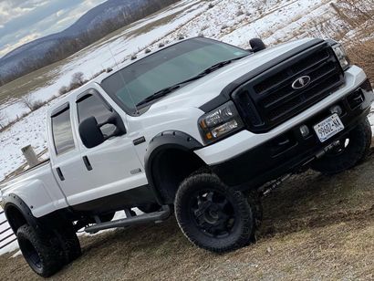 White lifted pickup truck with black trim, wheels, and tinted windows, parked on brown grass with a snowy mountain background. White lifted pickup truck with black trim, wheels, and tinted windows, parked on brown grass with a snowy mountain background.