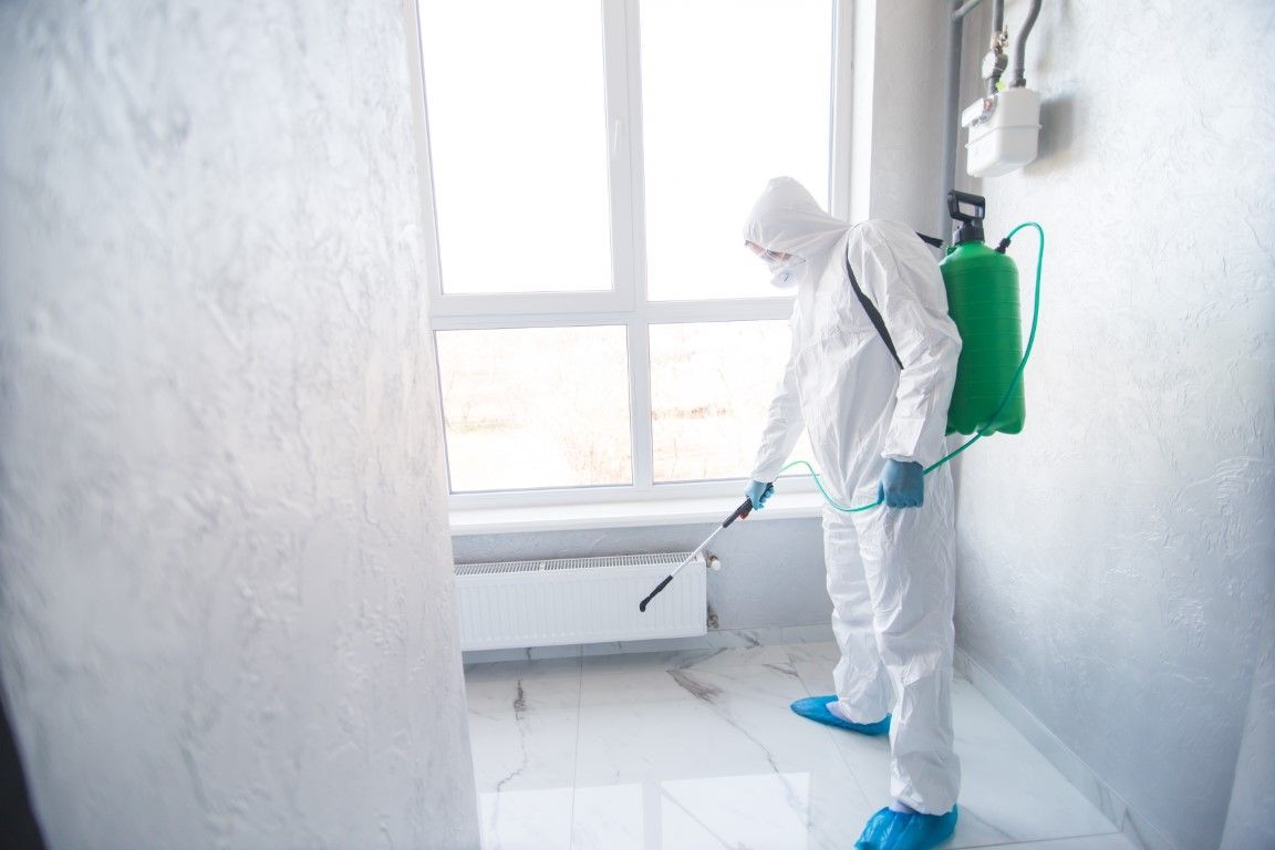 Person in hazmat suit spraying disinfectant in a room with a window.
