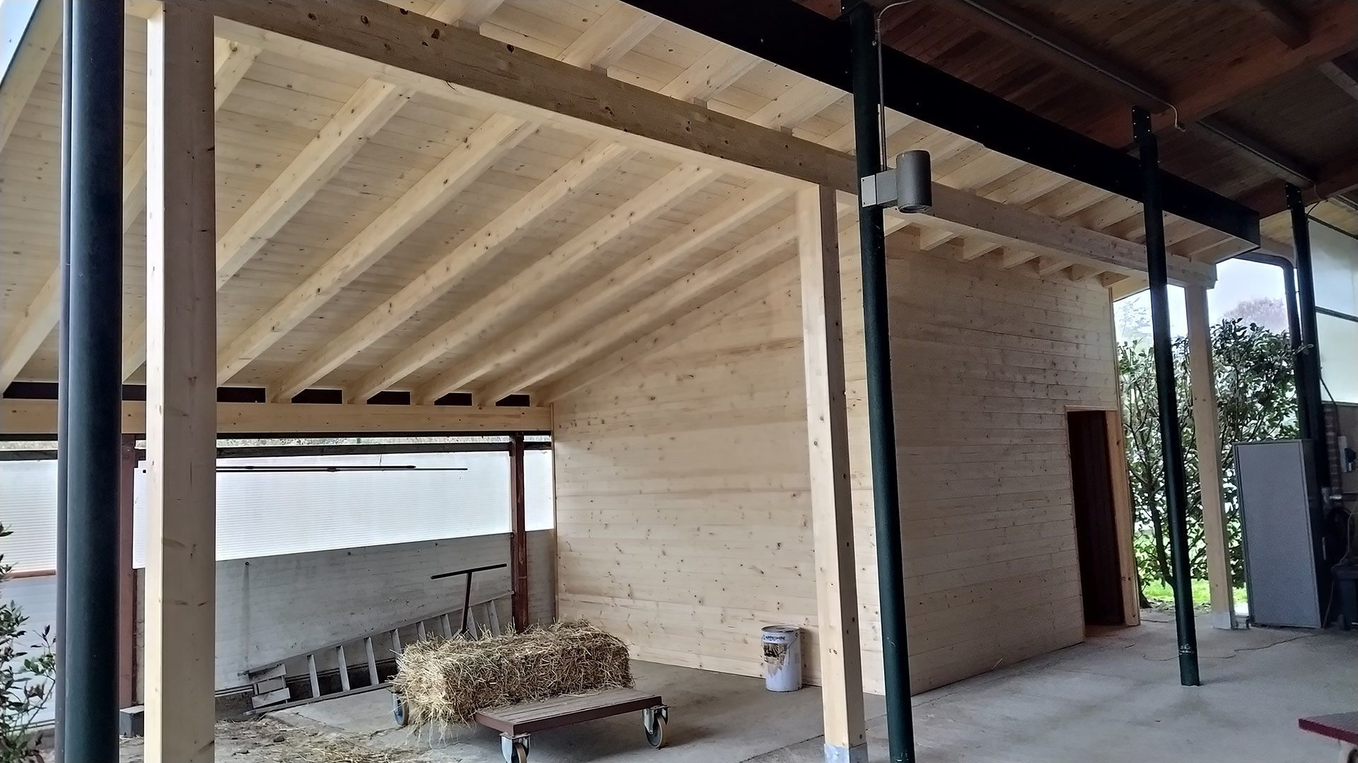 Patio coperto con travi in ​​legno e una piccola struttura in mattoni accanto a un muro e zona salotto esterna.