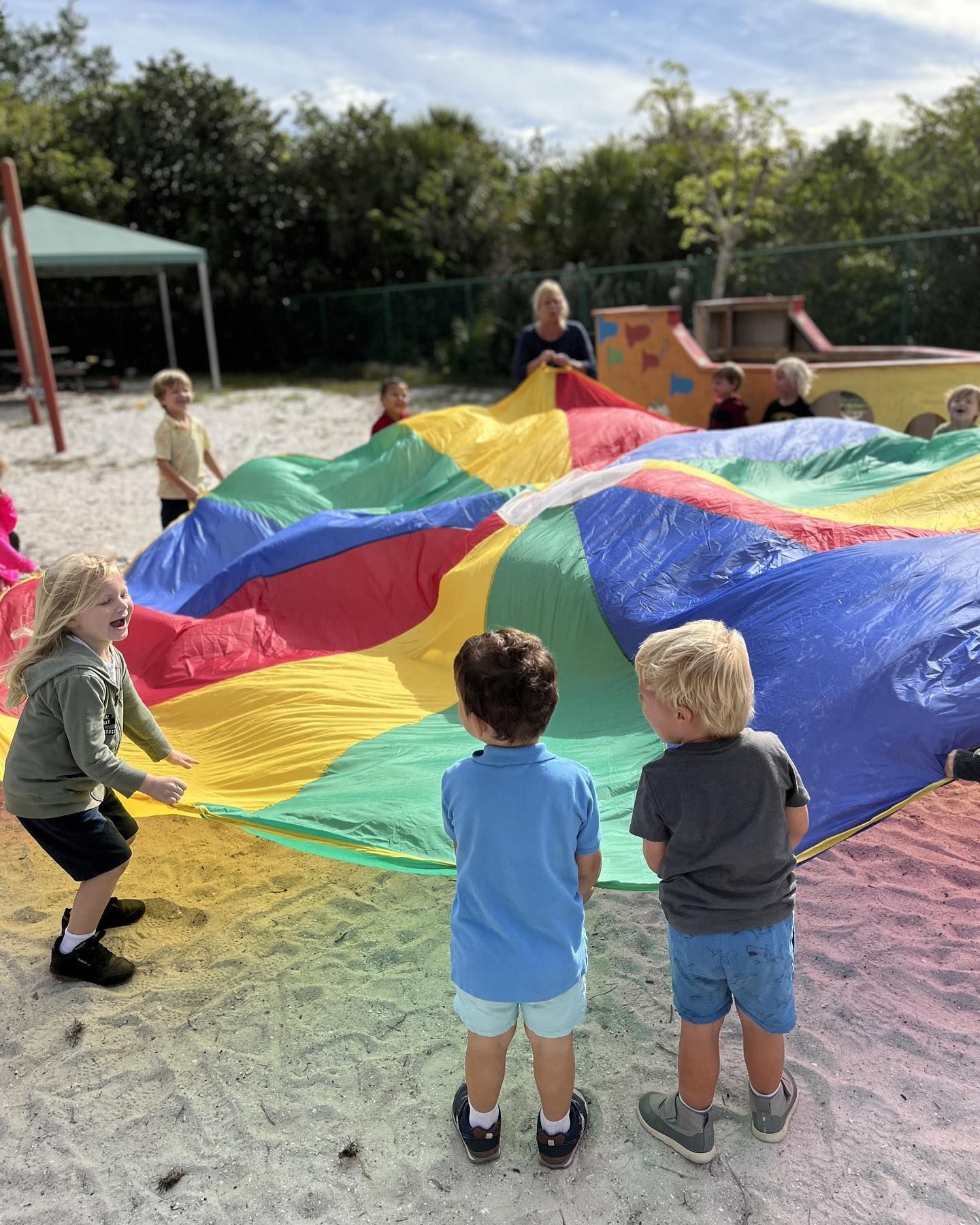 A group of children are playing with a colorful parachute in the sand.