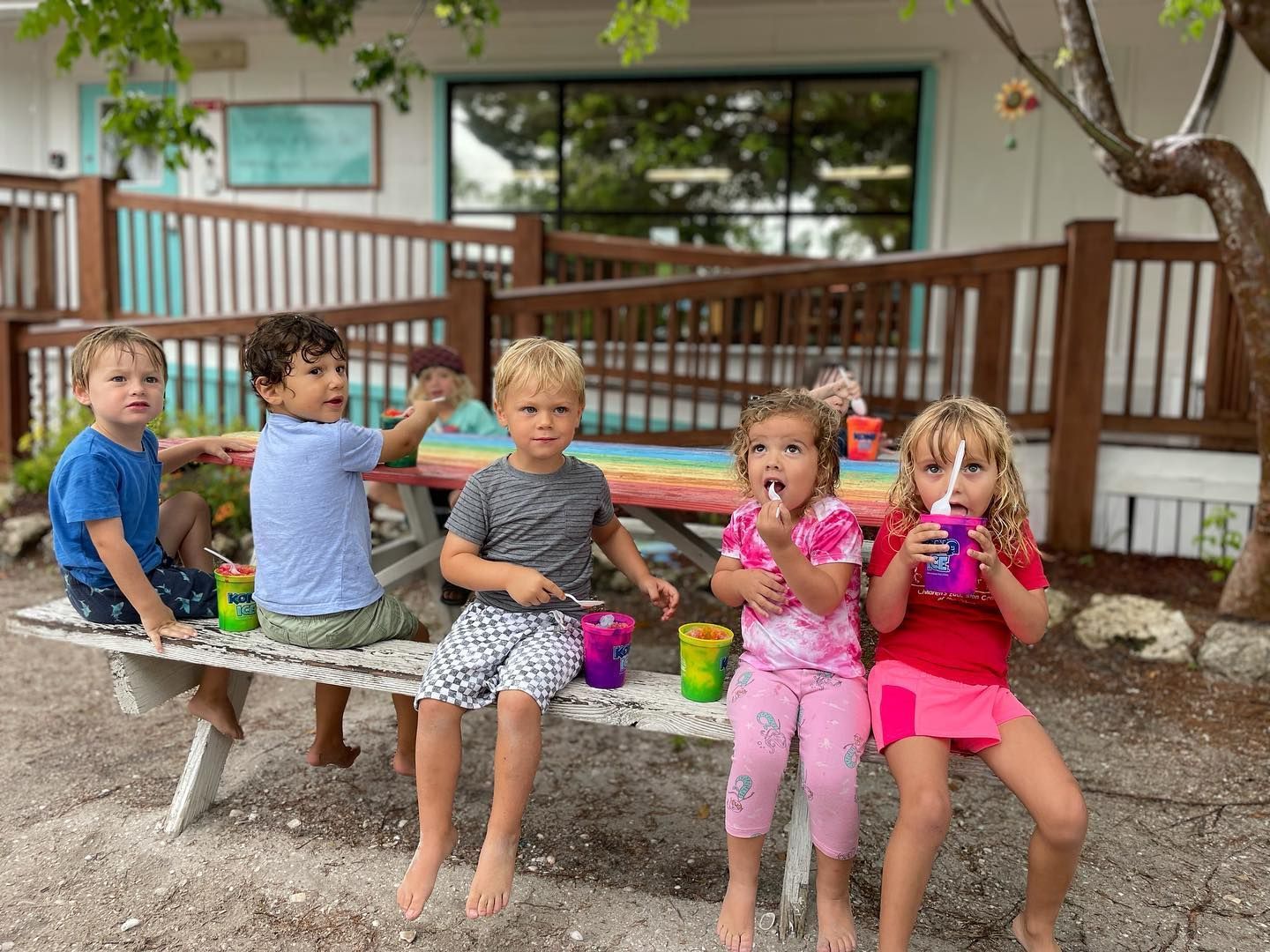 A group of children are sitting on a picnic table eating ice cream.