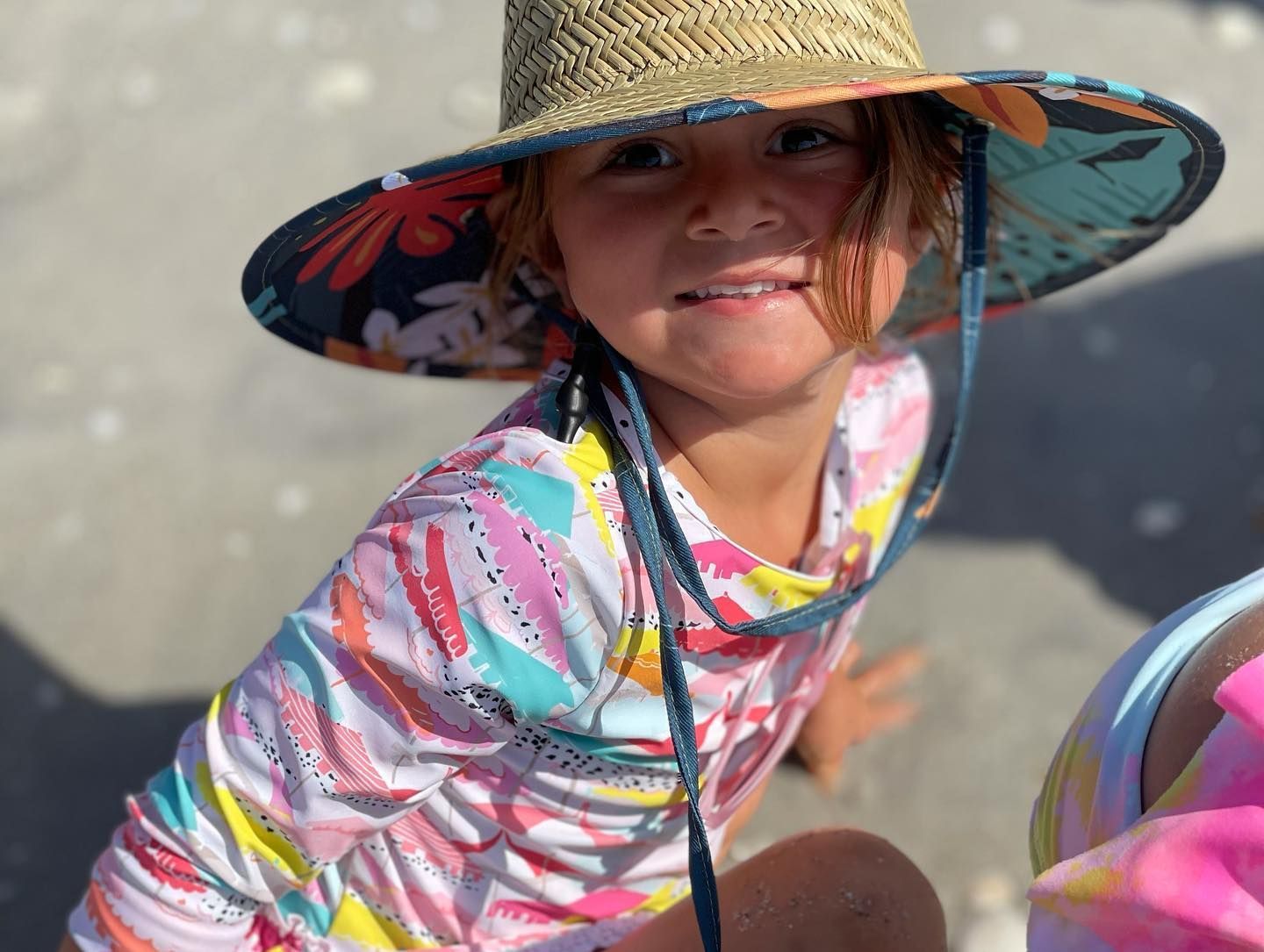 A little girl wearing a straw hat is sitting on the beach.