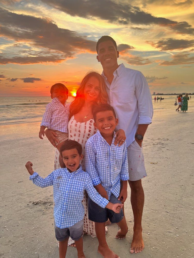 A family is posing for a picture on the beach at sunset.