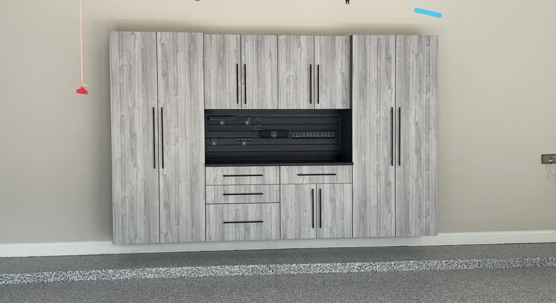 Gray wood grain garage cabinets with black recessed center section and drawers.