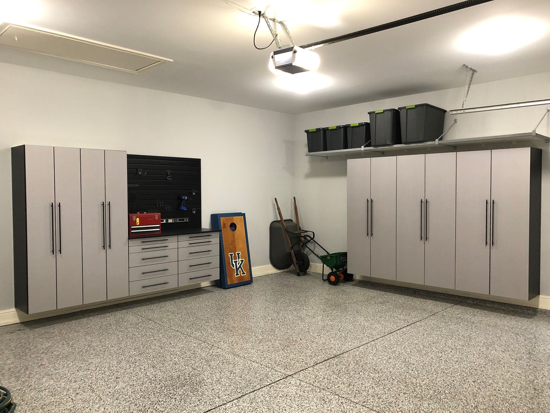 Garage with epoxy floor, storage cabinets, and various items like a lawn spreader, cornhole game, and wheelbarrow.