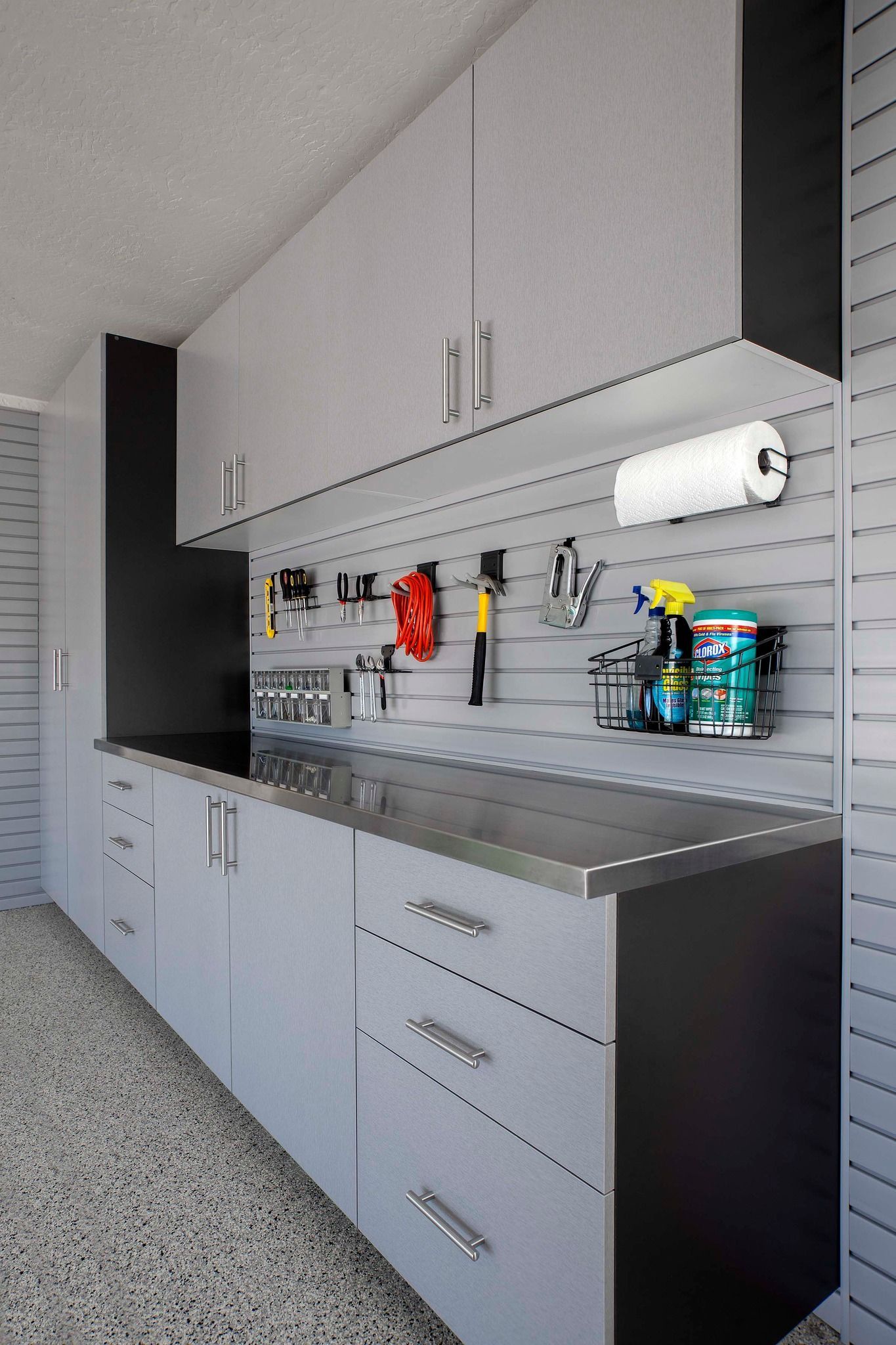 Garage with gray and black cabinets, stainless steel counter, and tools hanging on a slatwall.