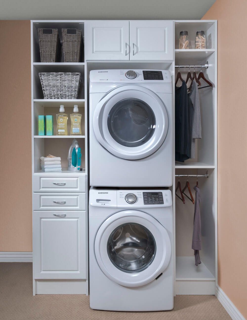 White laundry room organization unit with stacked washer and dryer, cabinets, and hanging rod.
