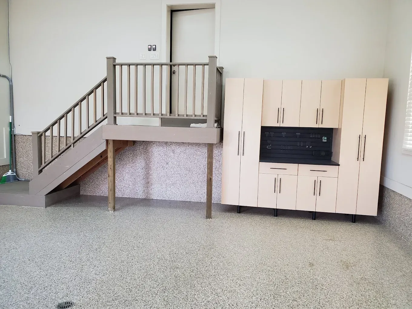 A garage with a set of stairs, a raised platform, and storage cabinets. The floor has a speckled pattern.