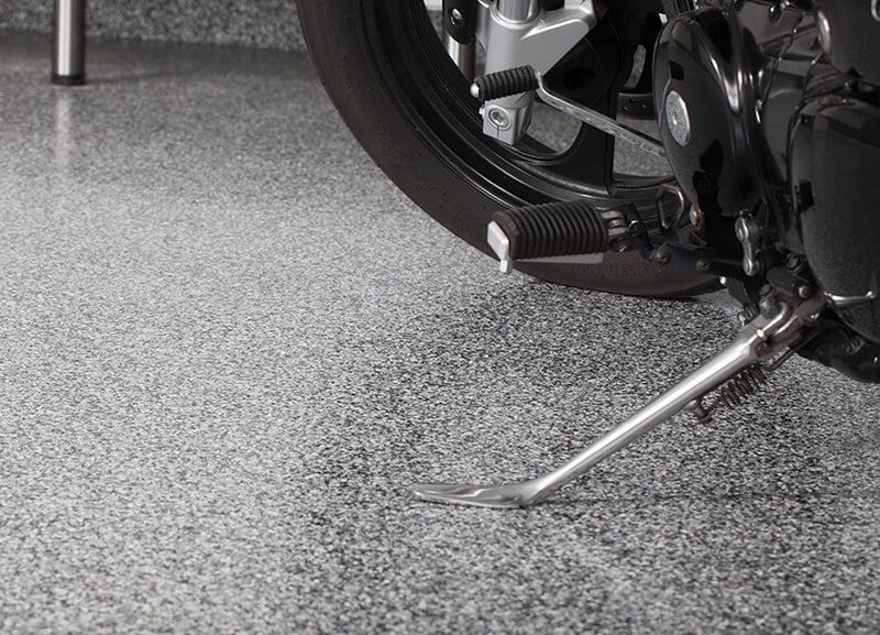 Motorcycle with side stand down on speckled gray epoxy garage floor.