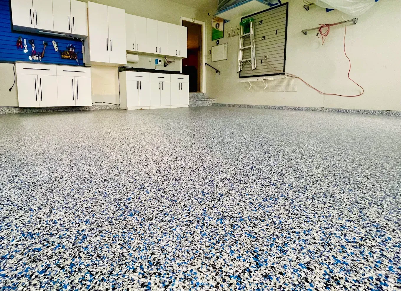 Garage with a speckled epoxy floor in blue, white, and gray. White cabinets line the back wall.