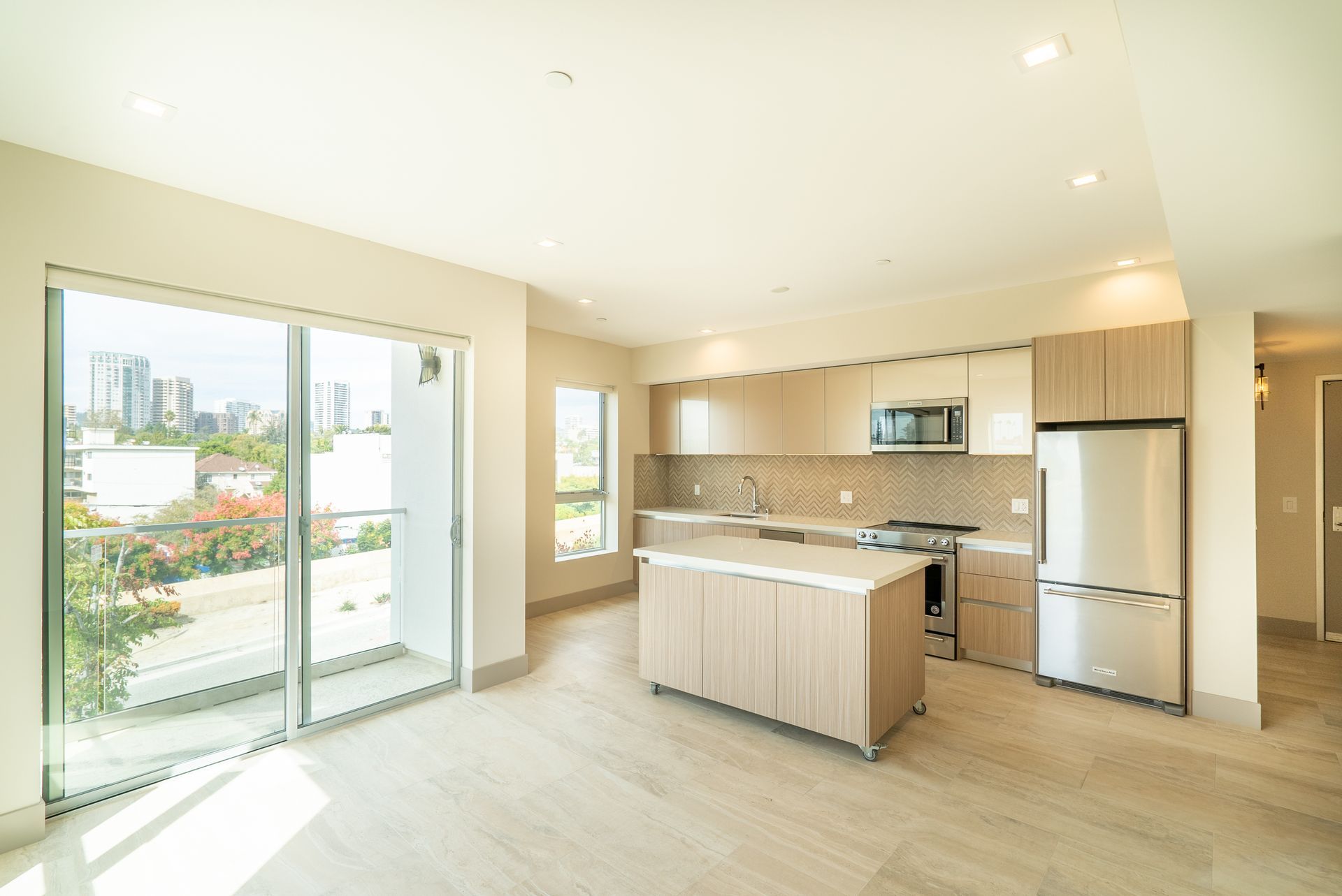 Spacious, modern kitchen with light wood cabinets, stainless steel appliances, and large sliding glass doors.