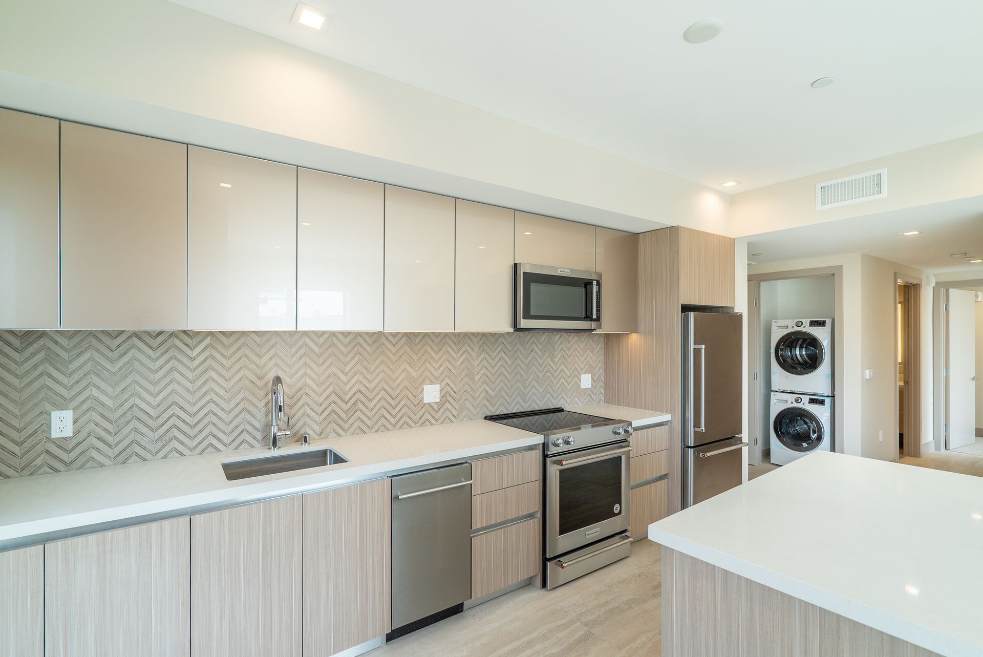 Modern kitchen with light wood cabinets, stainless steel appliances, and white countertops.