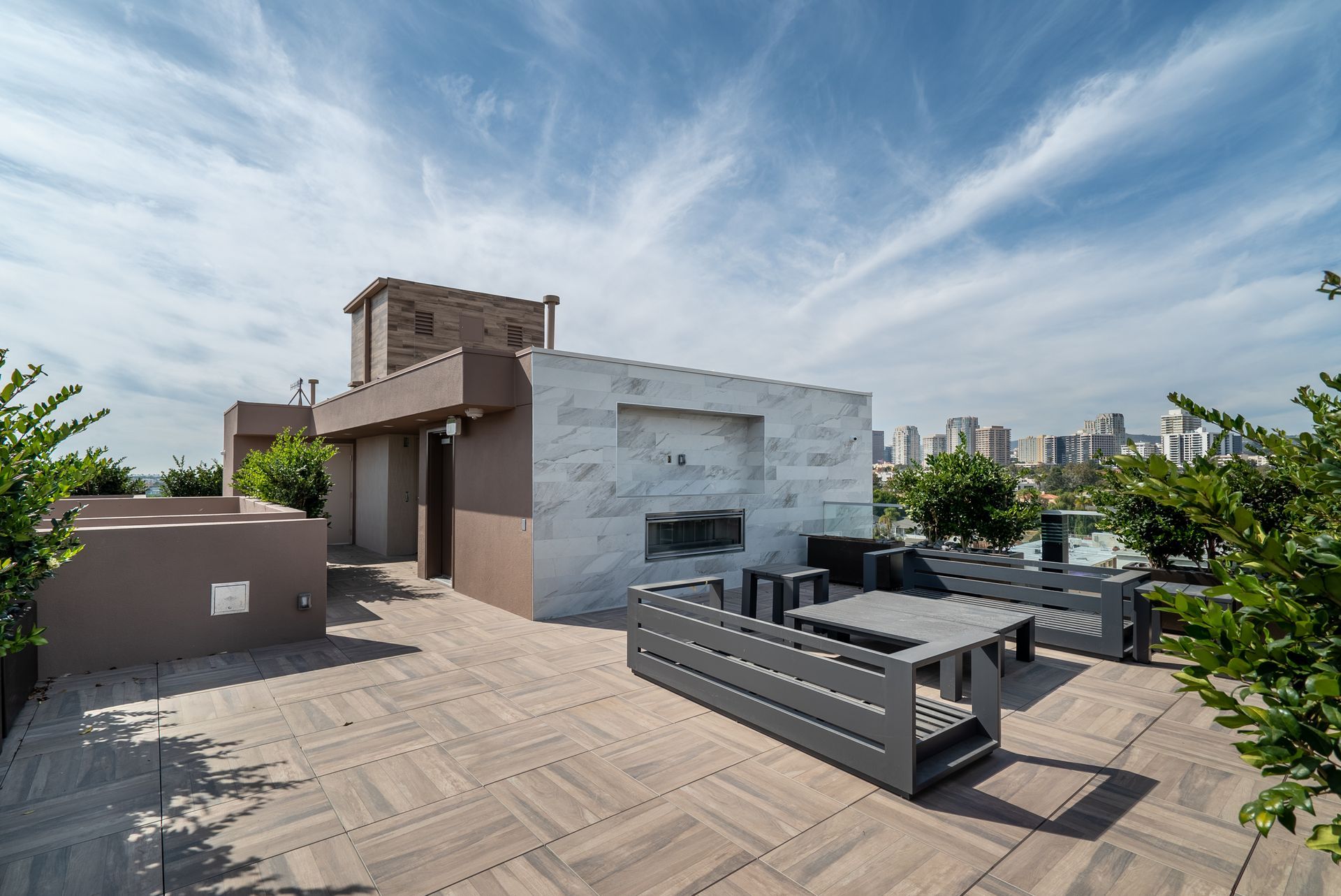 Rooftop patio with seating, fireplace, and city view under a blue sky with clouds.