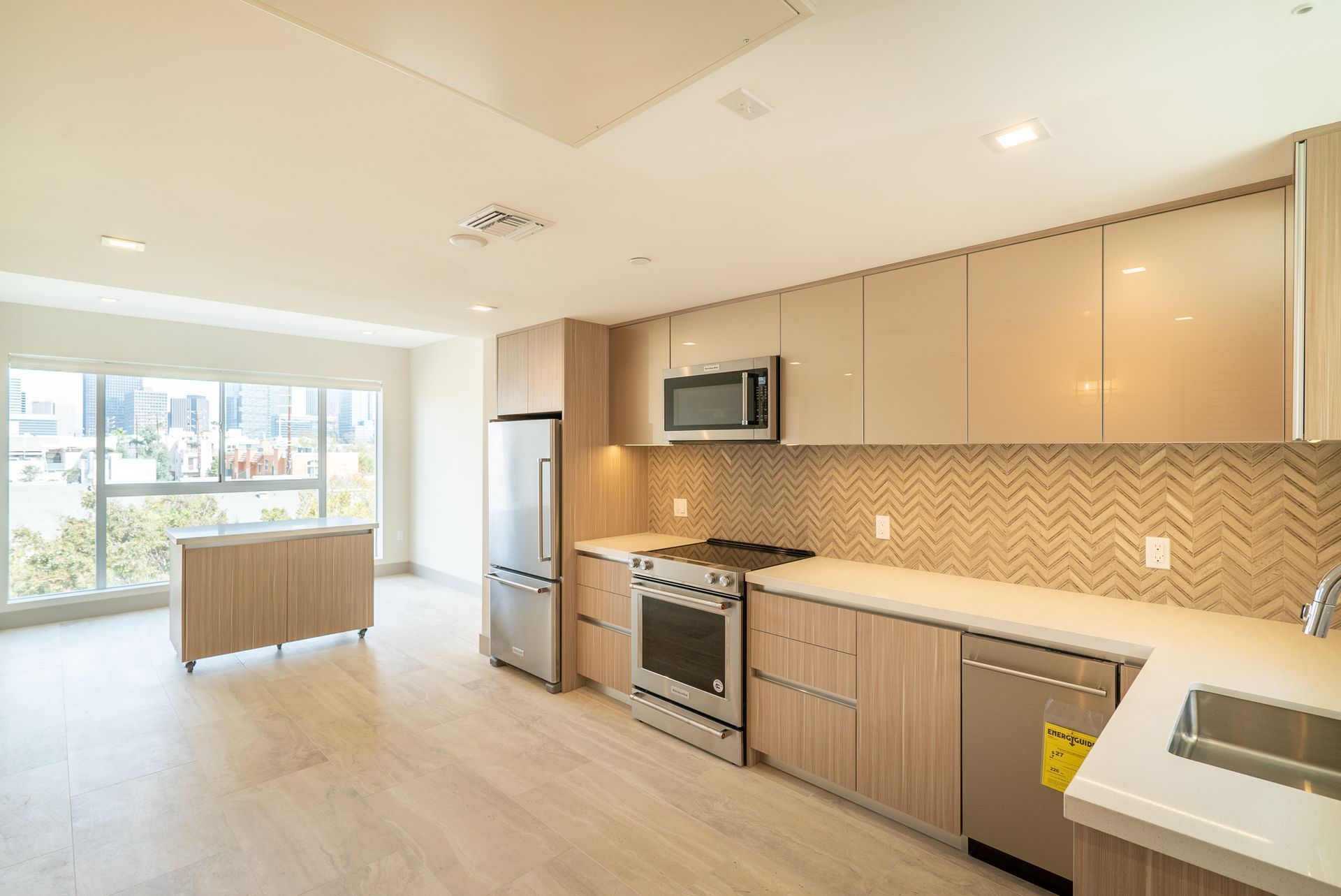 Modern kitchen with light wood cabinets, stainless steel appliances, and a large window.