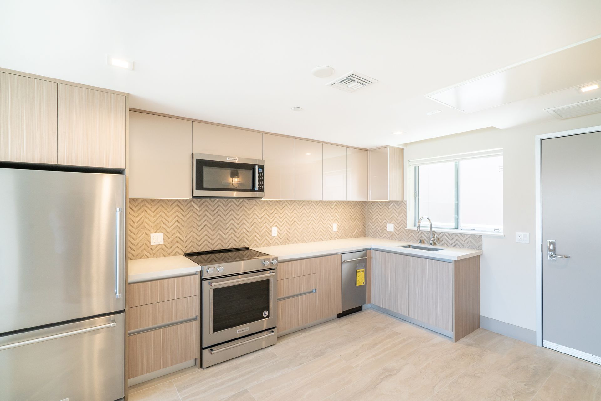 Modern kitchen with stainless steel appliances, light wood cabinets, and white countertops.