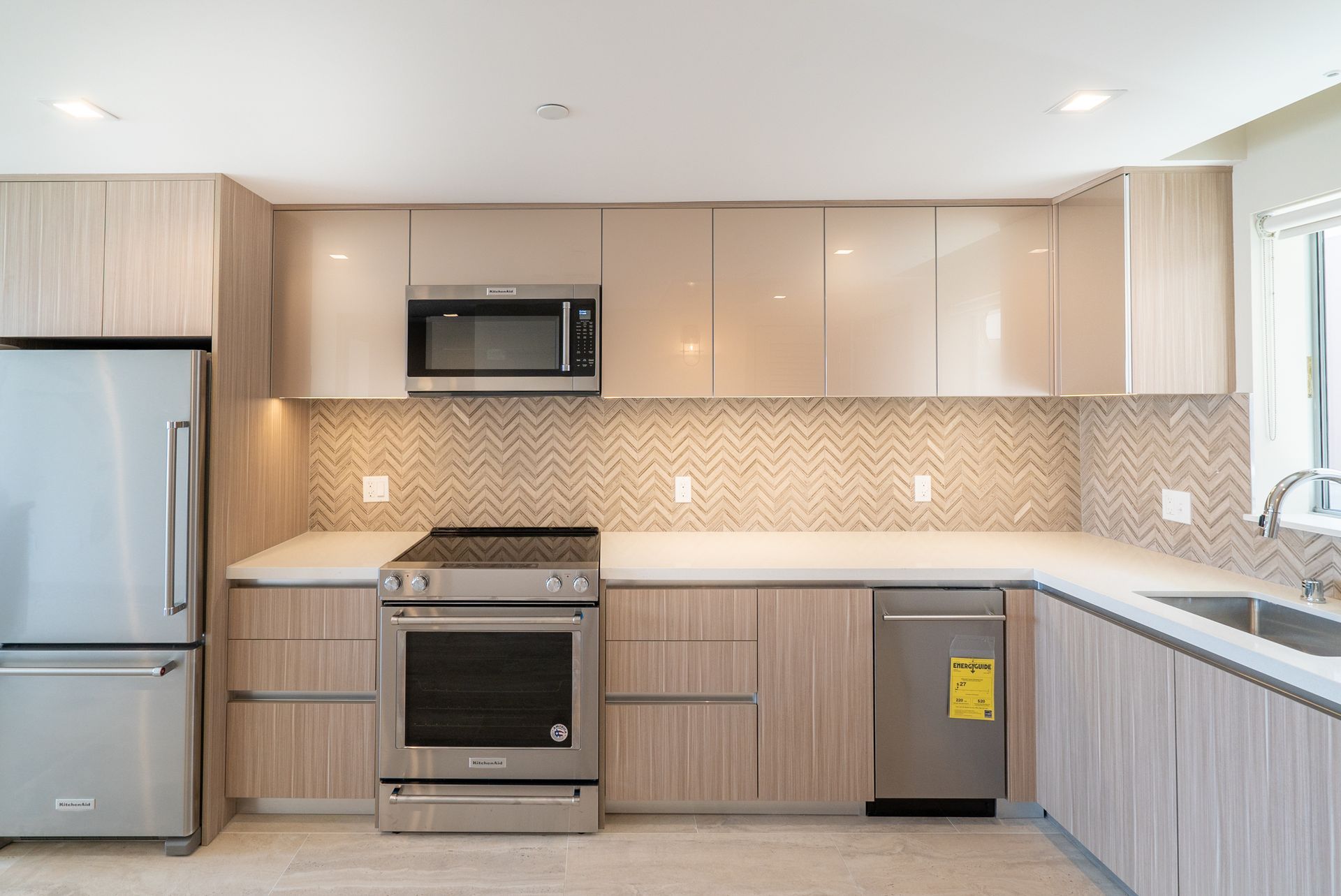 Modern kitchen with light wood cabinets, stainless steel appliances, and a tiled backsplash.