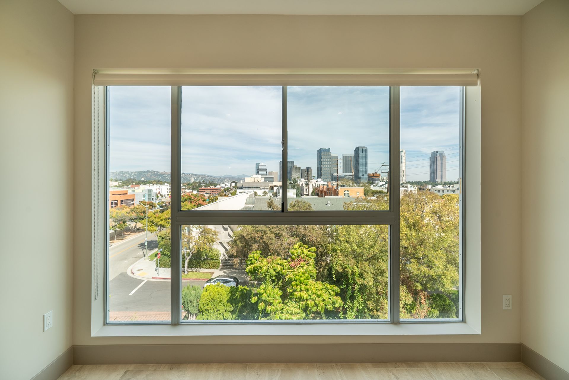 Large window overlooking a city. Green trees below, buildings and a blue sky above.