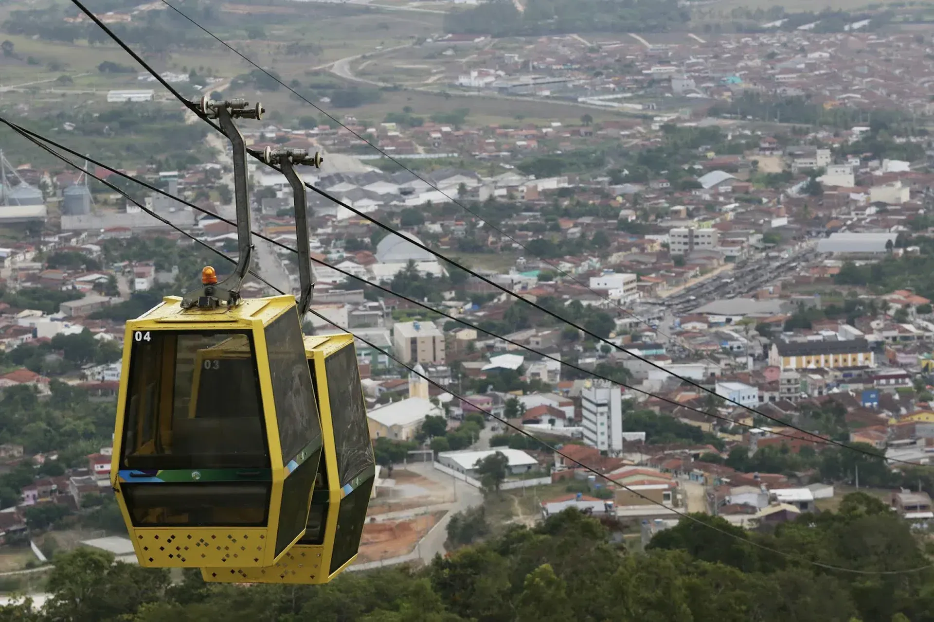 Um teleférico amarelo está passando por cima de uma cidade.