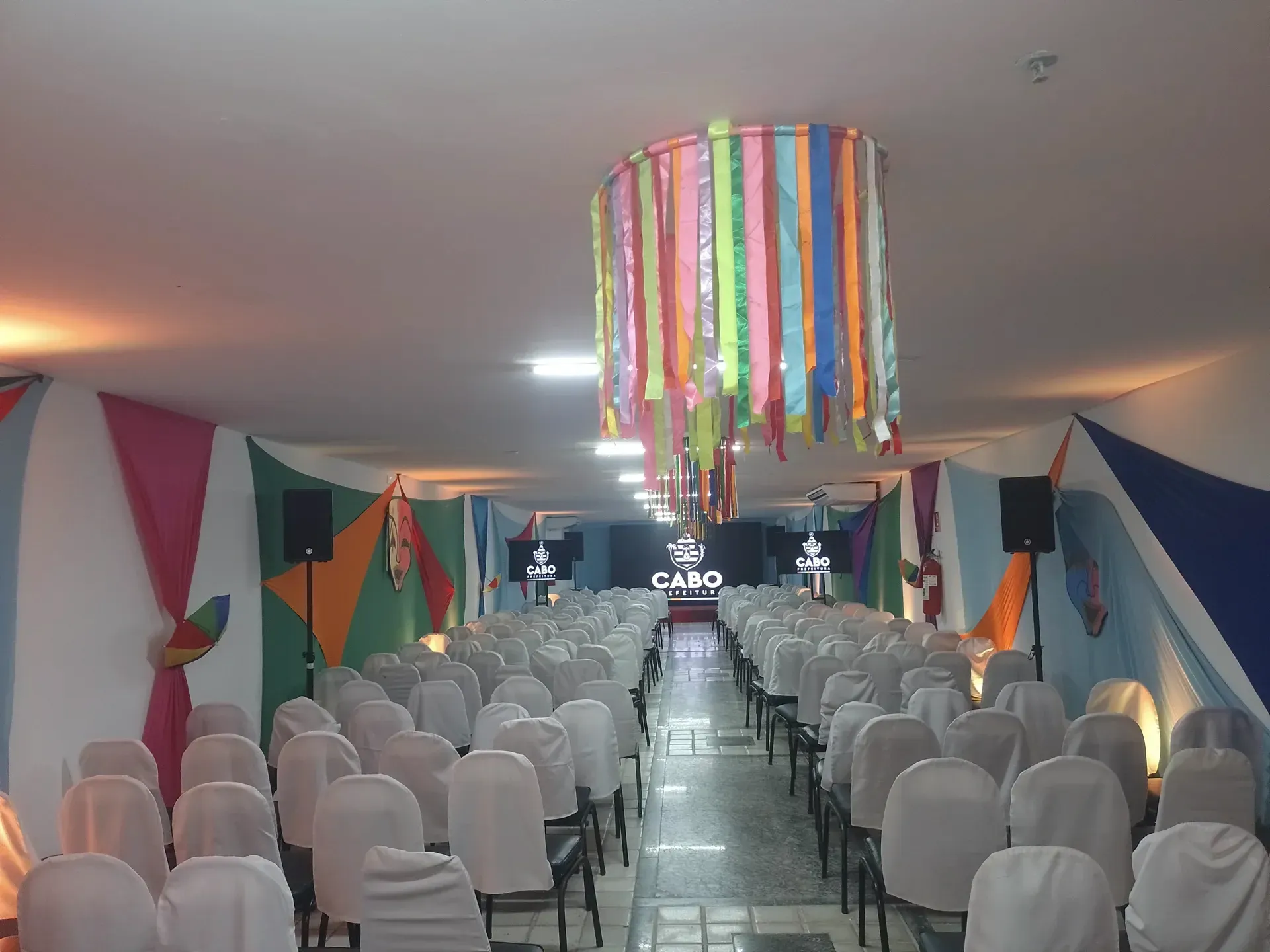 Uma sala comprida com fileiras de cadeiras e um lustre colorido pendurado no teto